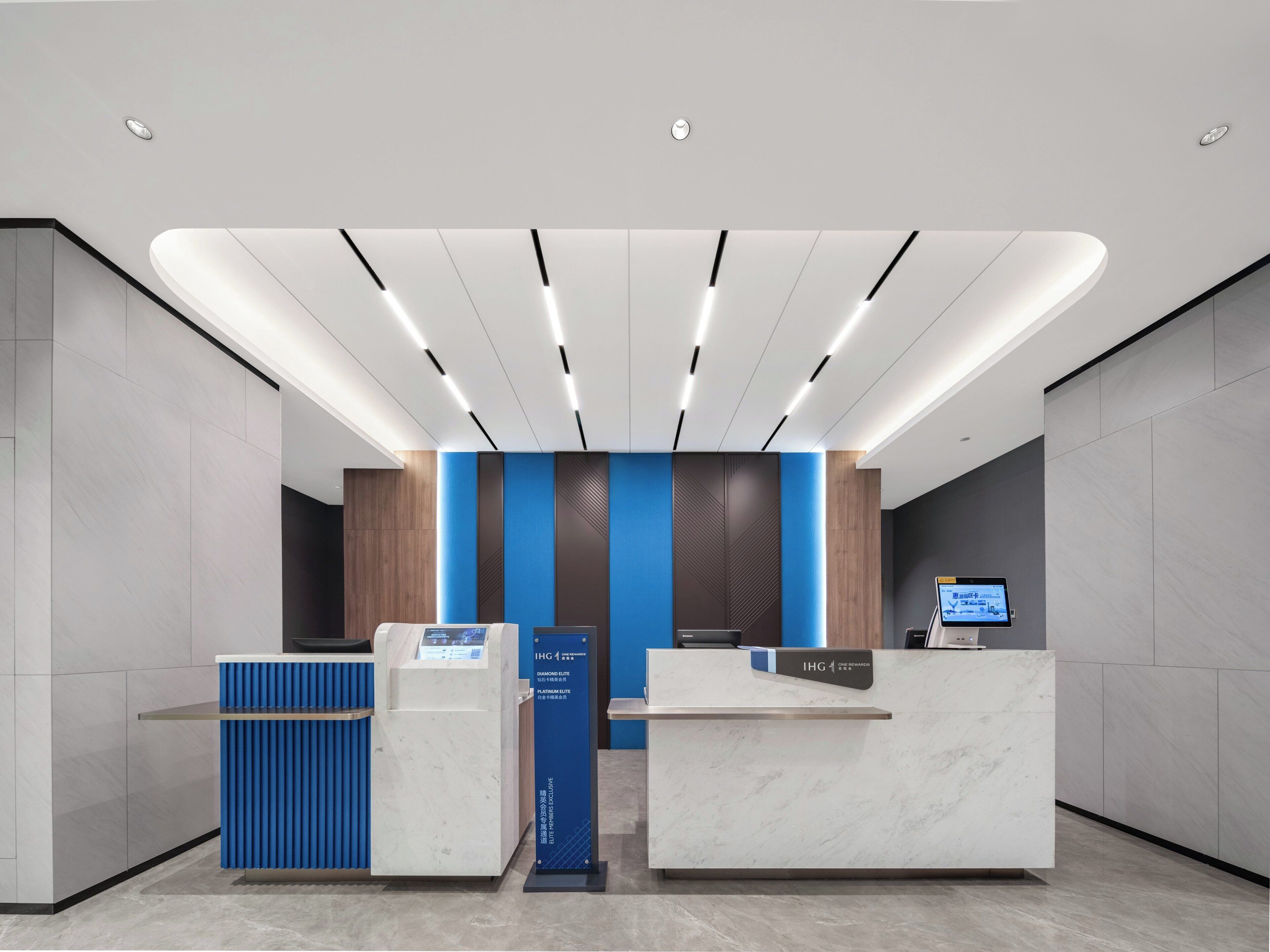 Un área de recepción moderna con dos mostradores, una pantalla digital y un expositor azul para información.
