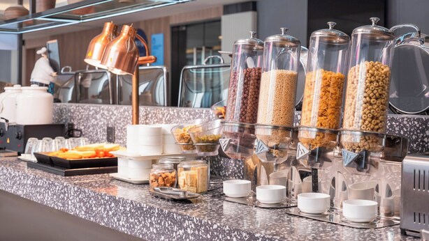 Zona de buffet con diversas opciones de comida y recipientes, incluyendo frascos de cereal y tazones.