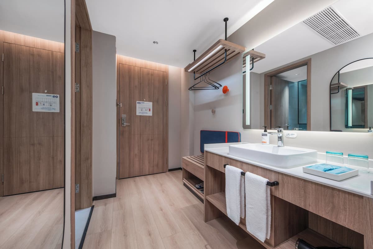 A modern bathroom with wooden cabinetry, a large mirror, and a dual sink vanity.
