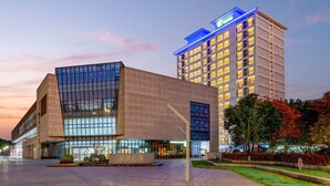 Un hotel moderno con una fachada de vidrio destacada y un edificio tradicional con letreros iluminados.