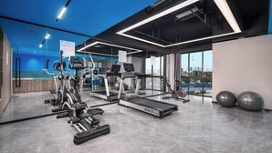 Un gimnasio moderno con diversos equipos de cardio y entrenamiento de fuerza, ventanas amplias y vistas a la ciudad.