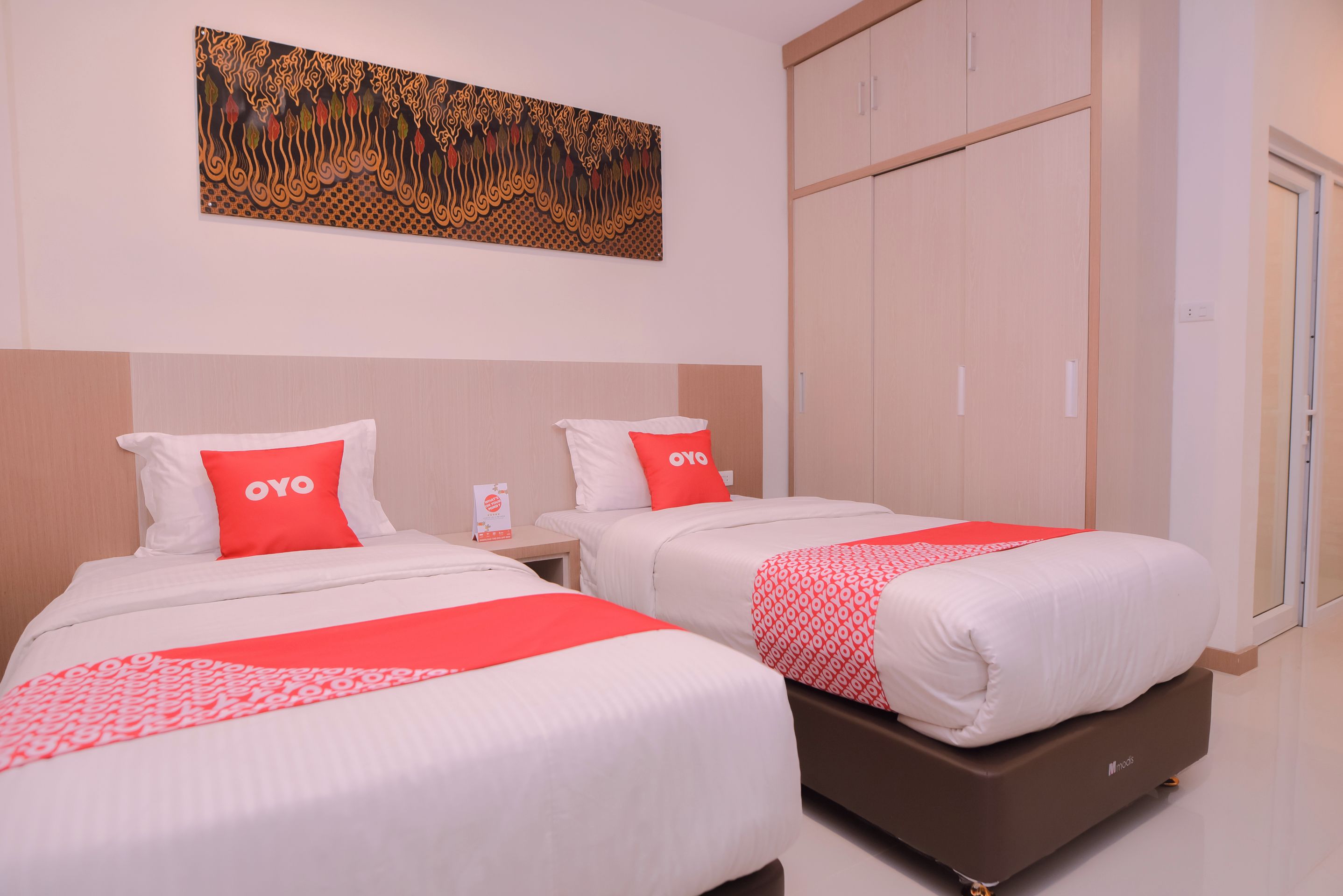 A hotel room with two beds, each with a white and red bedspread, and a large artwork above the beds.