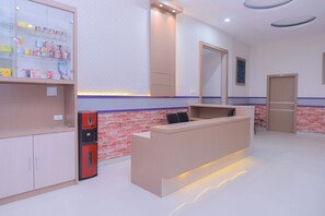 Un espace d’accueil comprenant un comptoir de réception, une vitrine réfrigérée contenant des collations, un mur décoratif en briques et un luminaire moderne.