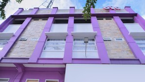 Un immeuble à plusieurs étages, doté d’une façade violette, de grandes fenêtres et d’une enseigne bien visible avec les lettres « OYO ».