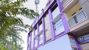 Een meerhoog gebouw met een paarse gevel, een zichtbaar bord voor een babywinkel, en een helder uitzicht op de lucht.