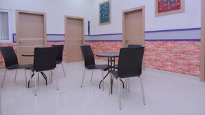 Een kamer met vier zwarte stoelen rond een kleine tafel, een muur met een baksteenmotief en twee deuren met een paarse streep.