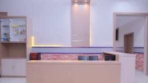 Een receptiebalie met een licht houten afwerking, een glazen vitrinekast links, en een metselwerk accentmuur erachter.