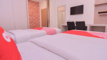 A hotel room with two beds, a desk, a television, and a brick wall.