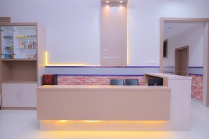 Een receptiebalie met een licht houten afwerking, een glazen displaykast aan de linkerkant en een geaccentueerde bakstenen muur achter de balie.