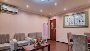 A room with a wooden floor, beige sofas, a wooden coffee table with a floral centerpiece, and a framed calligraphy piece on the wall. - Greentree Inn Beijing Yuegezhuang Hotel (Beijing)