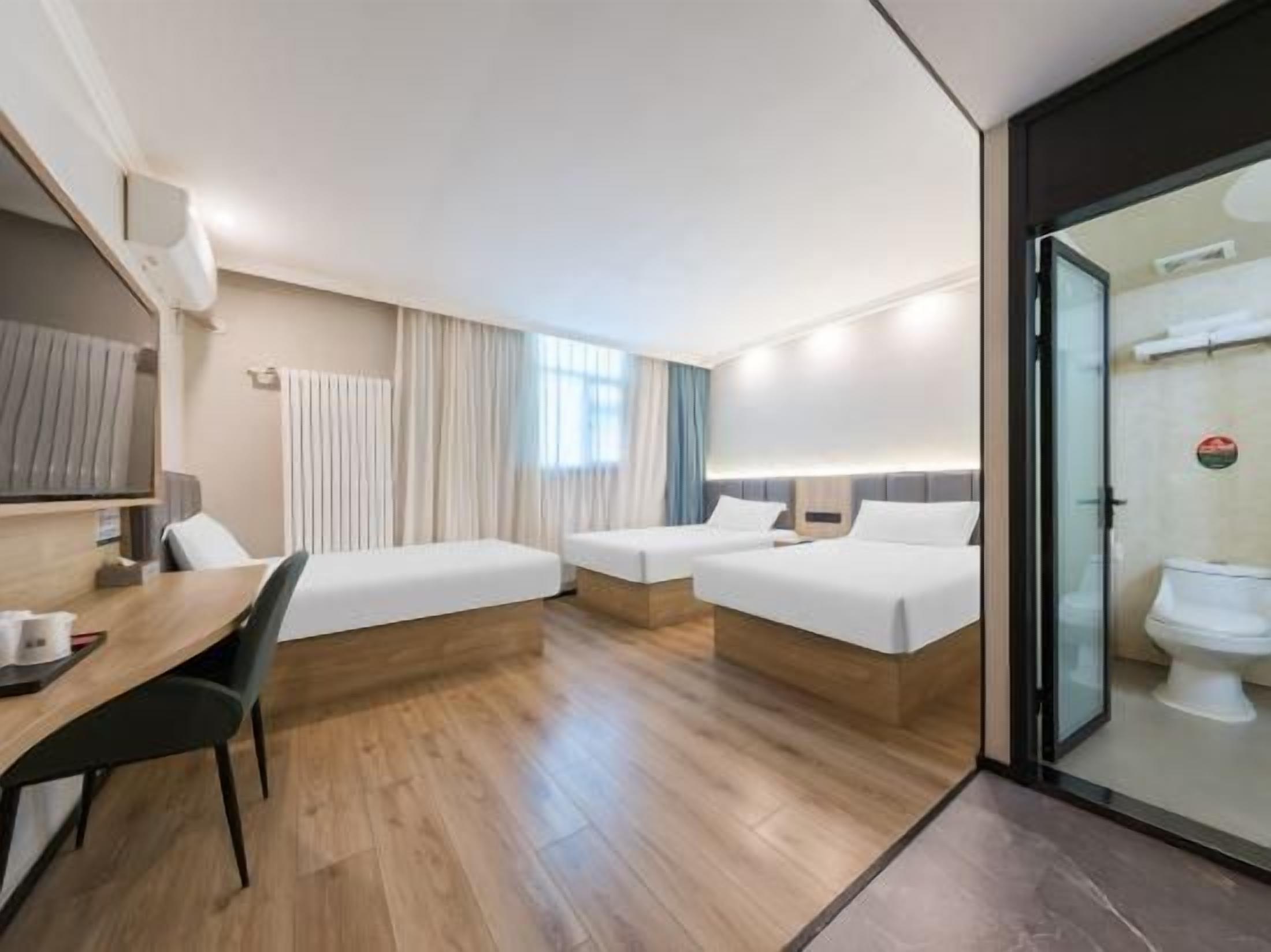 A hotel room with two beds, a desk, and a glass partition separating the room from the bathroom.