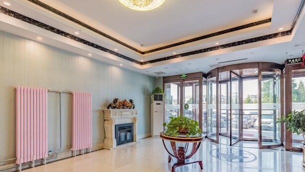 A spacious lobby with a fireplace, a glass elevator, and a potted plant. - Greentree Inn Beijing Yuegezhuang Hotel (Beijing)