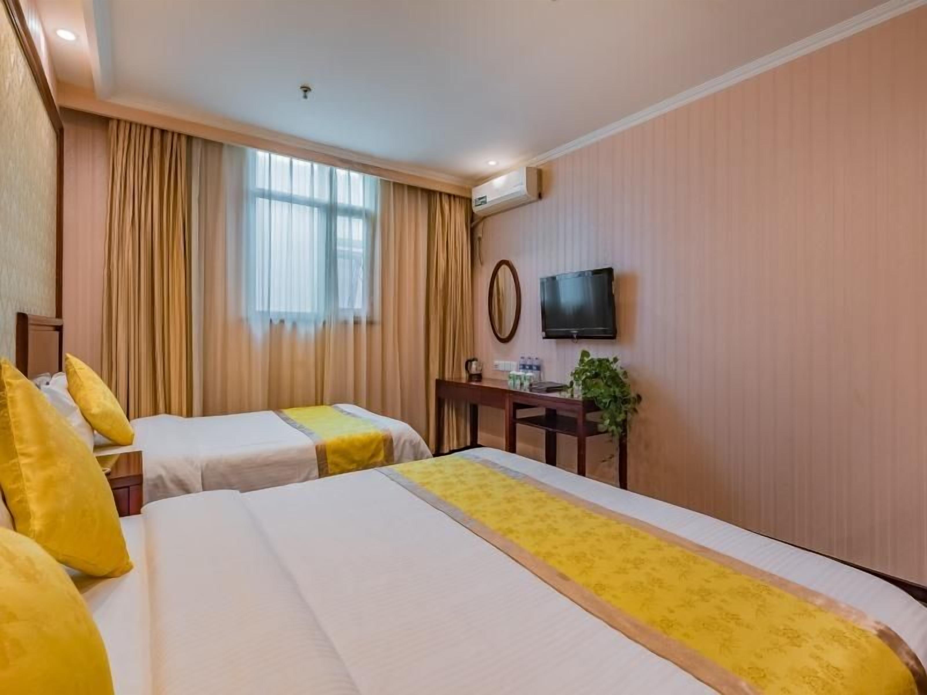A hotel room with two beds, a desk, a television, and a window with curtains.