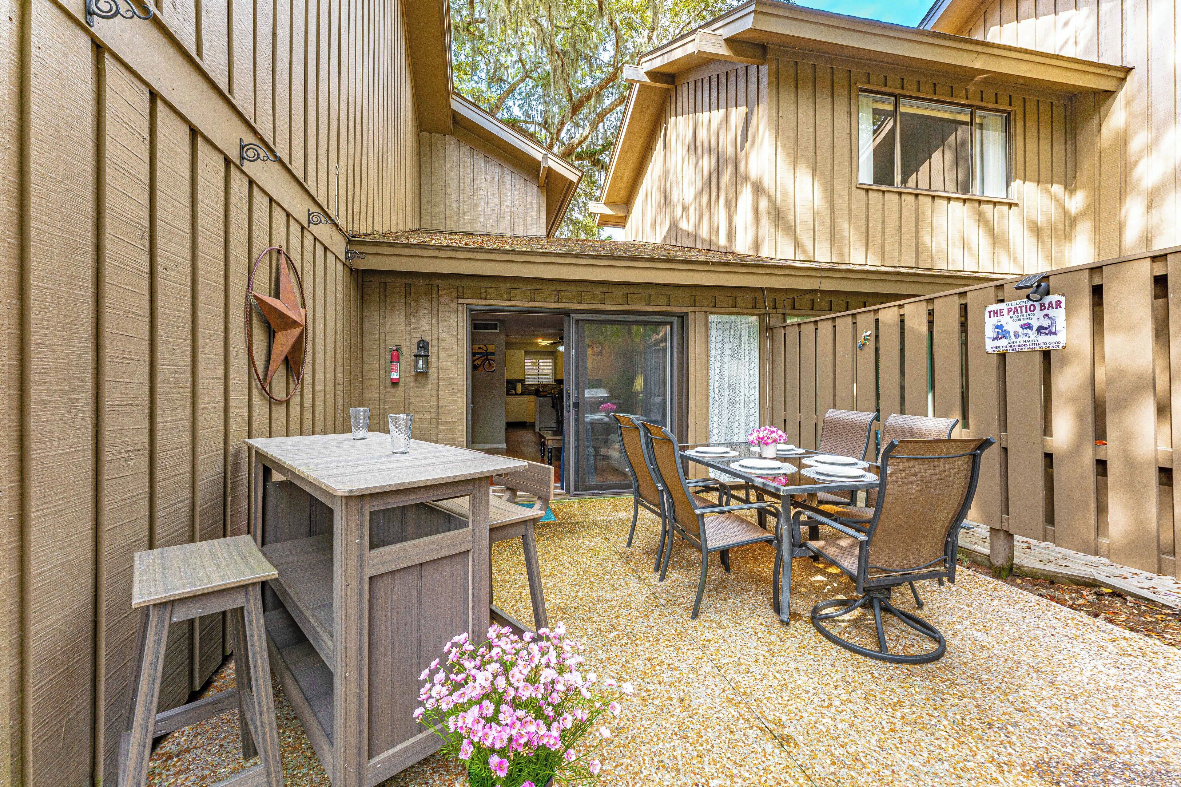 A patio area with a table and chairs, a wooden fence, and a sign for 'The Patio Bar'.