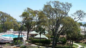 A pool area with a view of the ocean, surrounded by trees and a building with a green roof. - Palmetto Dunes Ocean-View Villa w/ Balcony, Jacuzzi,  Golf, Dolphin Tour & Beach Gear Included (Hilton Head Island)