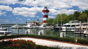 A marina with boats docked, a lighthouse, and a waterfront walkway with flowers. - Panoramic Ocean Views! Breakers Condo Steps to Dining & Shops (Hilton Head Island)