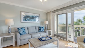 A modern living room with a grey sofa, two matching side tables, a coffee table, and a large window with a view of the outdoors. - Panoramic Ocean Views! Breakers Condo Steps to Dining & Shops (Hilton Head Island)