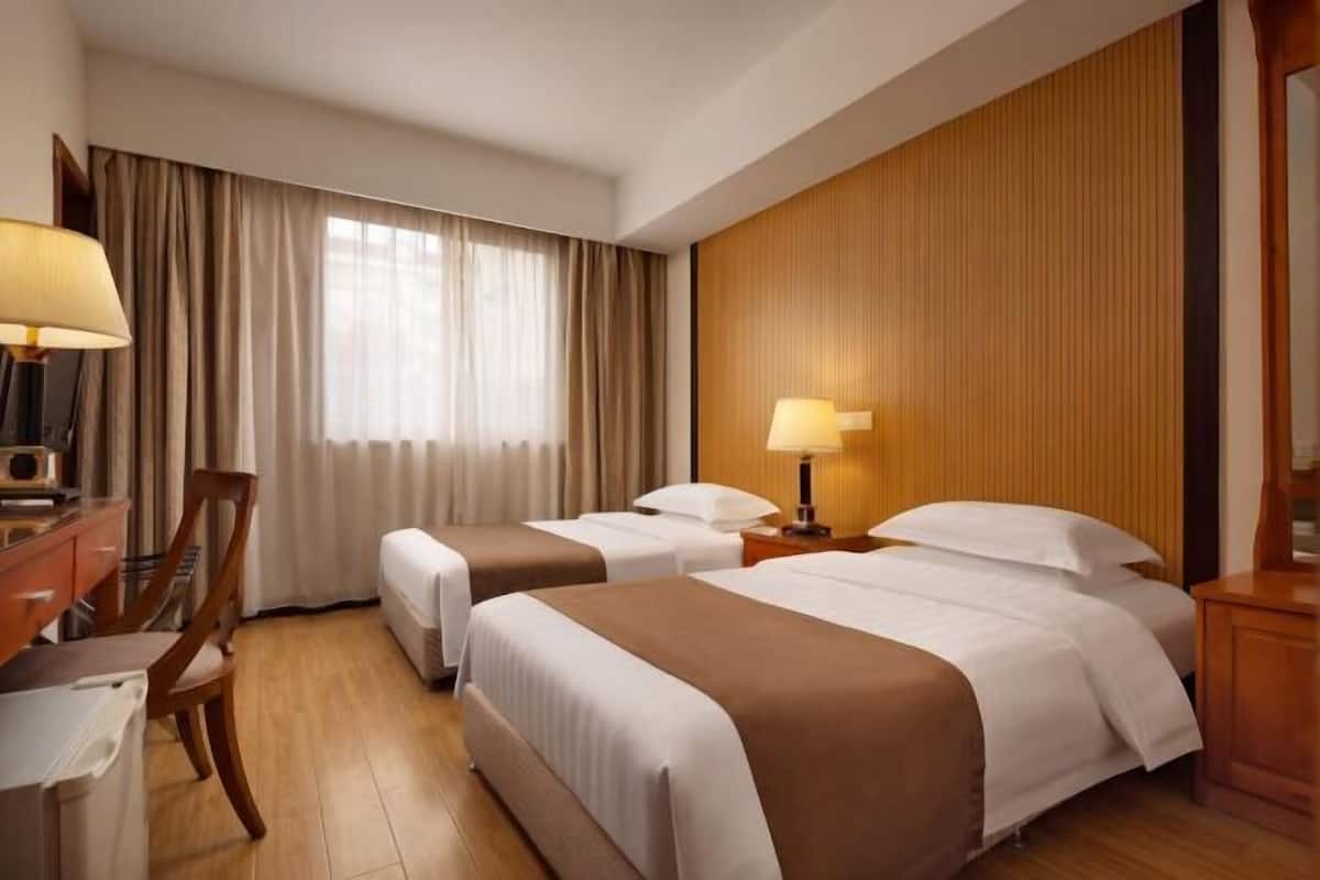 A hotel room with two beds, a desk, a chair, and a large window with curtains.