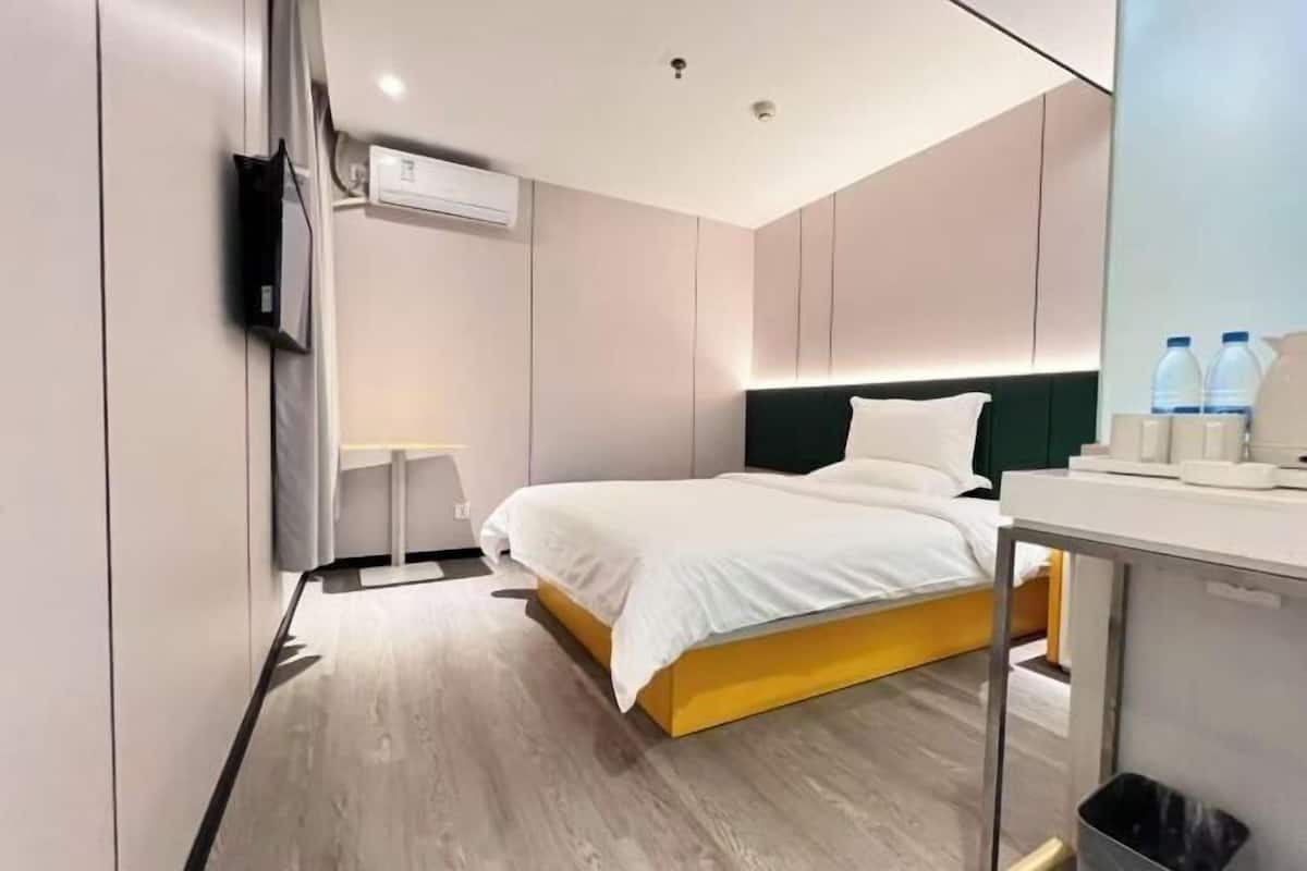 A modern hotel room with a bed, bedside table, and a small desk with a chair.
