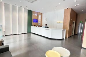 Zona de recepción de un hotel con mostrador, un reloj y una pantalla digital.