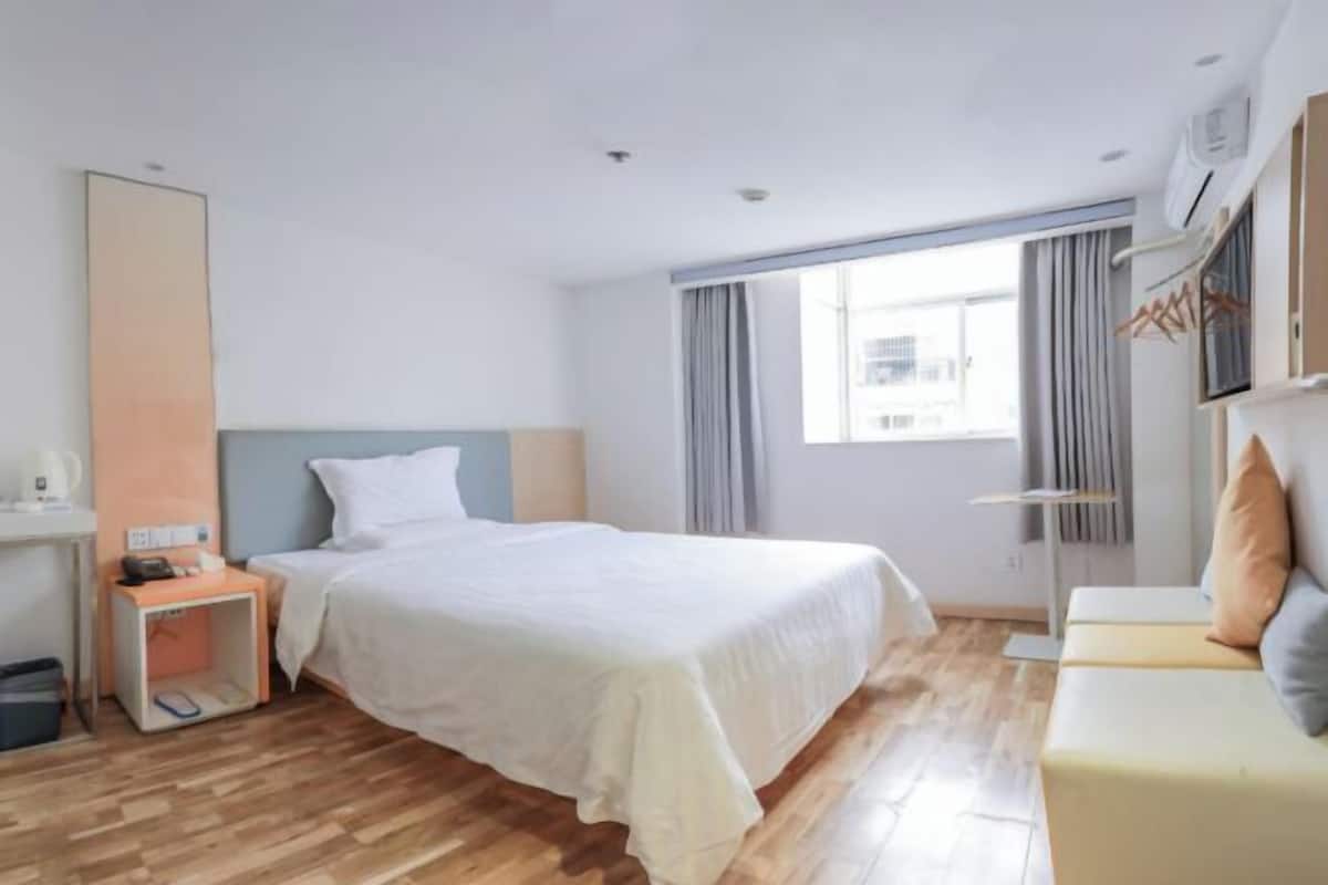 A hotel room with a bed, a bedside table, a wardrobe, a sofa, and a large window.