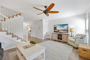 Ein geräumiges Wohnzimmer mit Treppe, Deckenventilator, Fernseher und einer gemütlichen Sitzecke.
