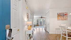 Un couloir avec une porte blanche, une lampe fixée au mur et un ventilateur de plafond.
