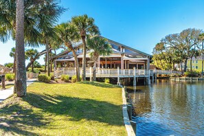 A waterfront property with a covered deck, palm trees, and a dock extending into a body of water.