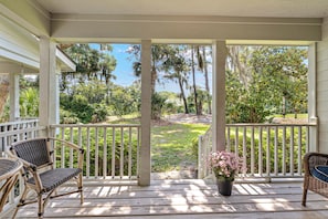A covered porch with wicker furniture, a potted plant, and a view of a landscaped yard.