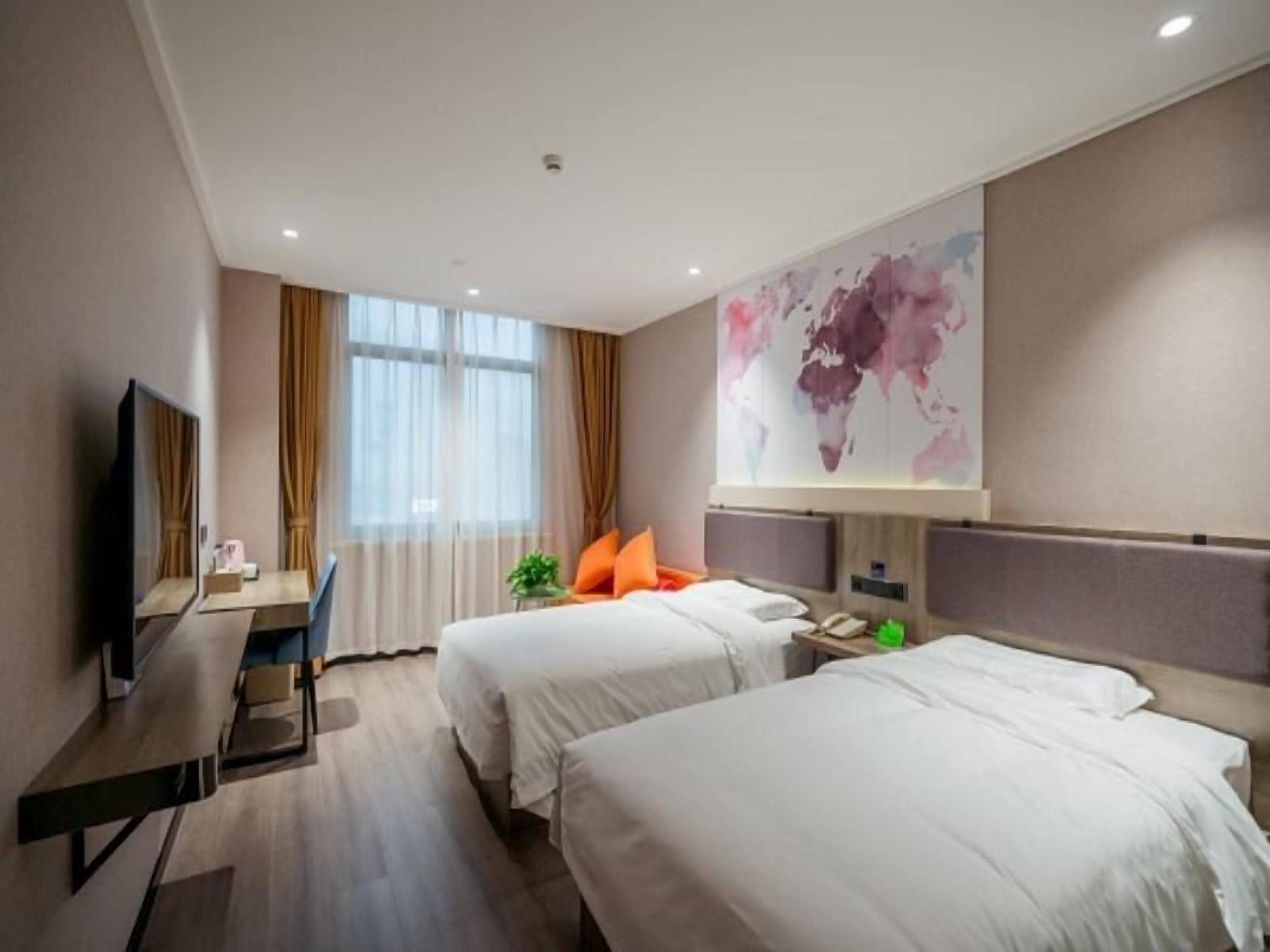 A hotel room with two beds, a desk, a television, and a world map on the wall.