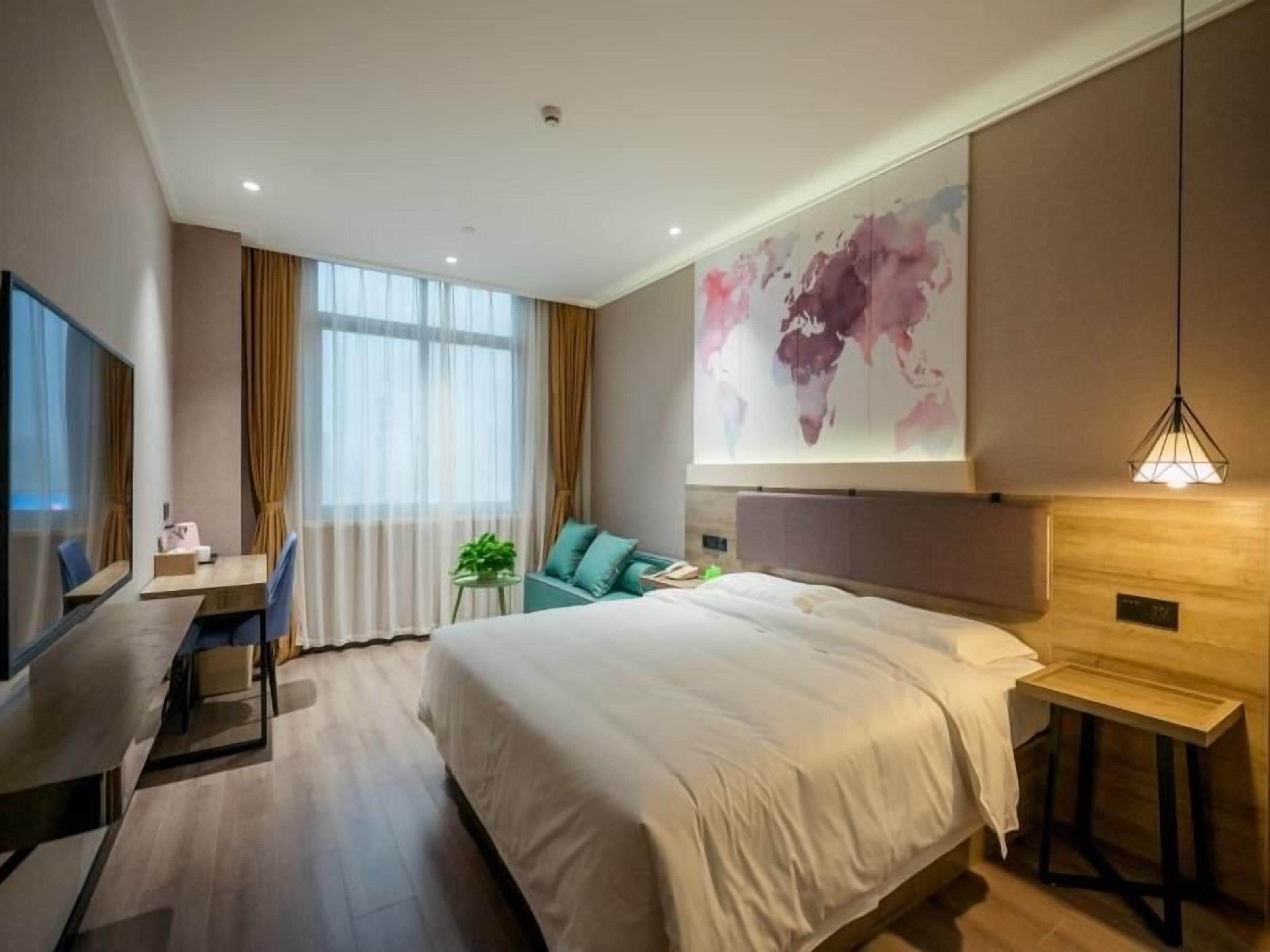 A modern hotel room with a large bed, a desk, a chair, a TV, and a world map on the wall.