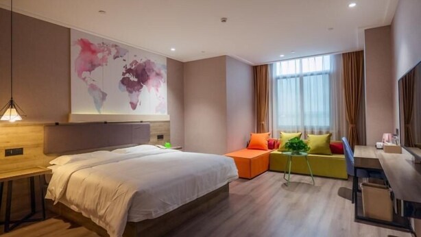 A modern hotel room with a large bed, a seating area with colorful cushions, a desk, and a large abstract wall art piece. - Vatica Hotel Wuxi Yixing Renmin Road (Wuxi)