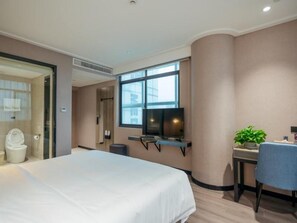 Une chambre d’hôtel avec un lit, un bureau et une chaise, une télévision et une fenêtre.