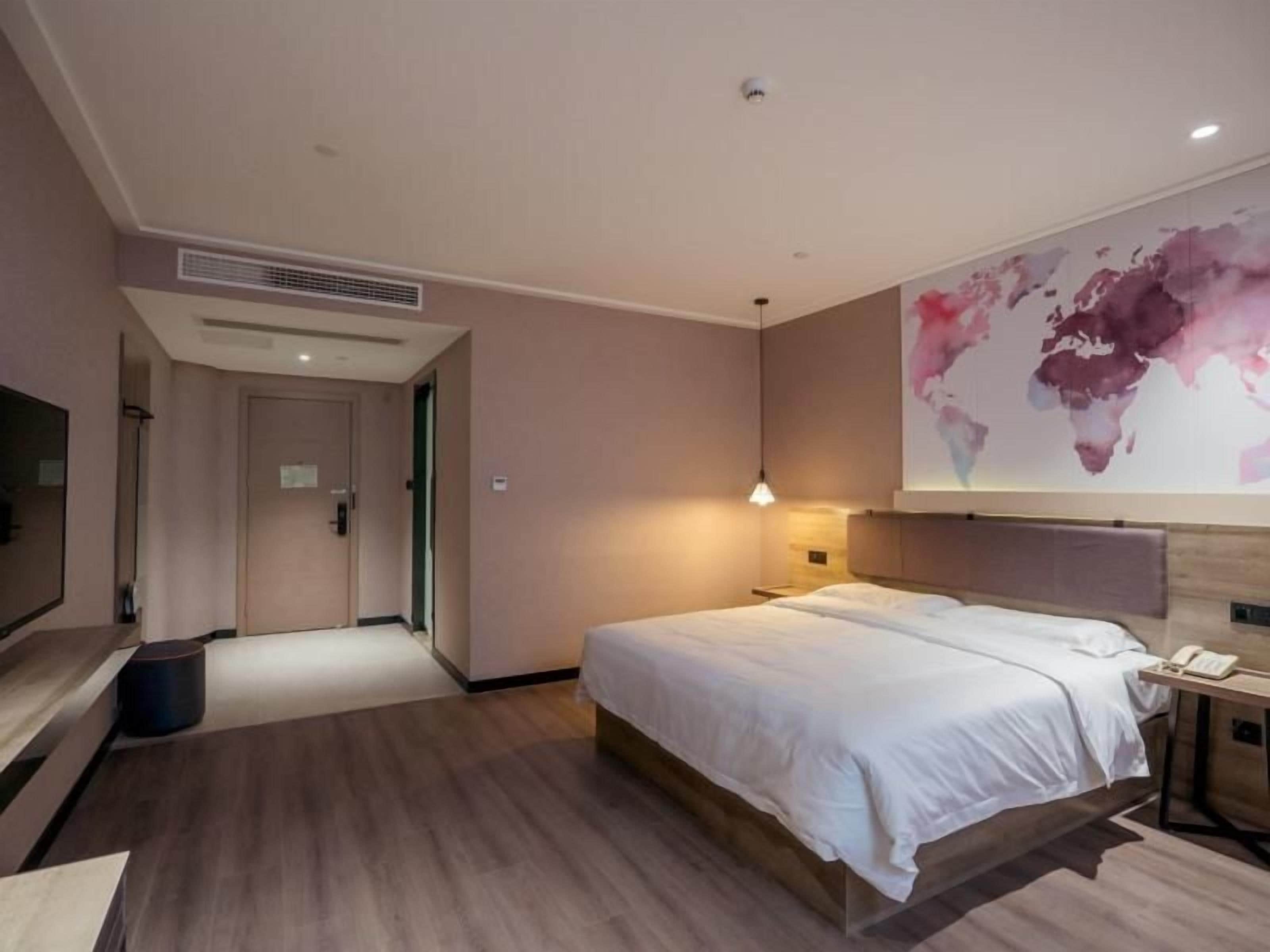 Una habitación de hotel moderna con una cama grande, un televisor de pantalla plana, un mural de un mapa mundial y piso de madera.
