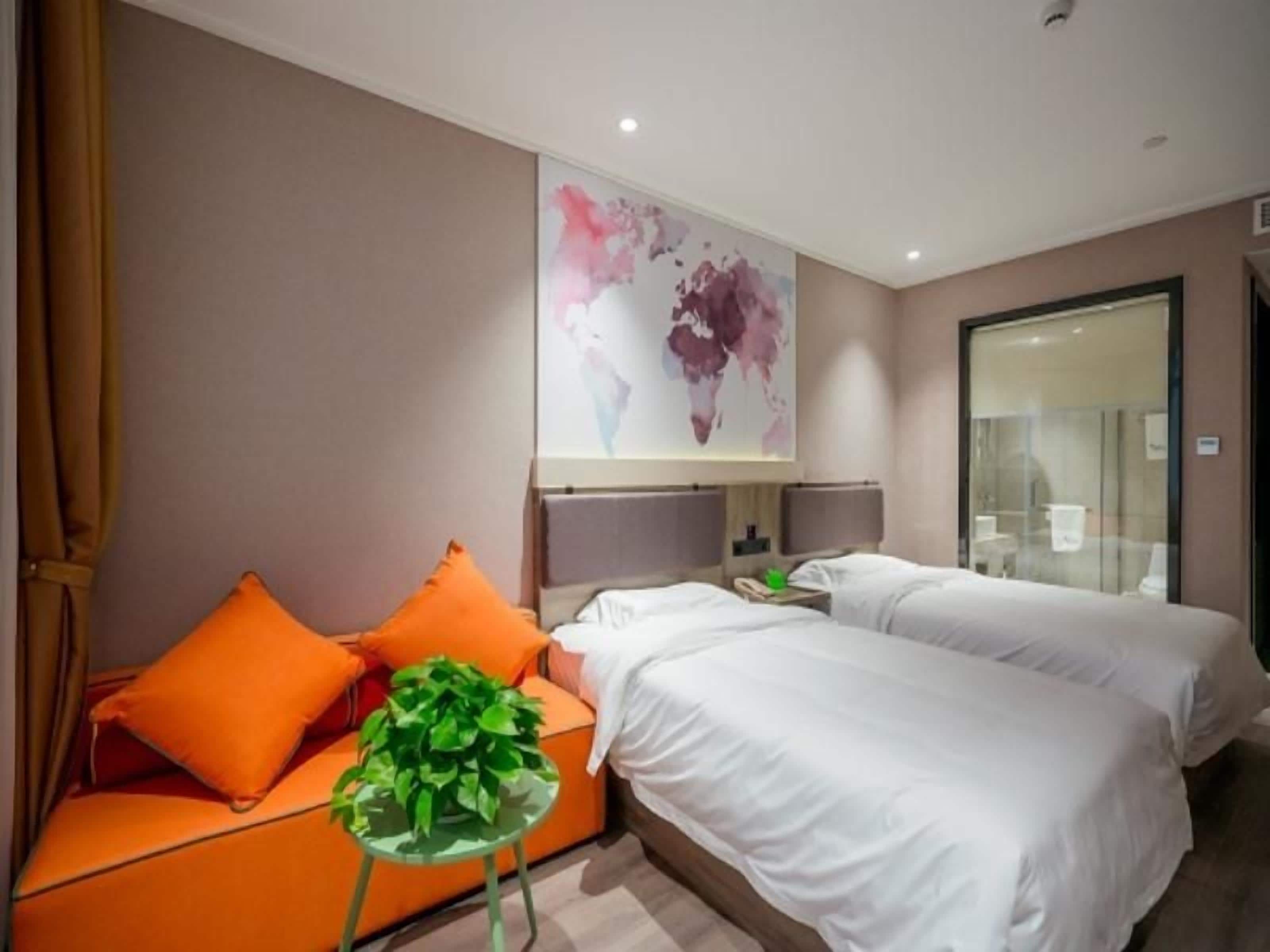 A hotel room with two beds, a sofa, a small table with a plant, and a world map on the wall.