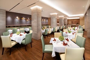Ein Restaurant mit mehreren Tischen, grünen Stühlen und modernem Interieur.