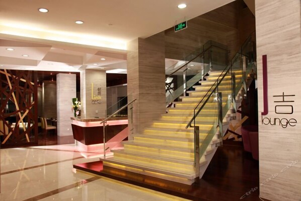 Een moderne lobby met een receptiebalie, een trap met glazen leuning en een muur met de tekst "J lounge".