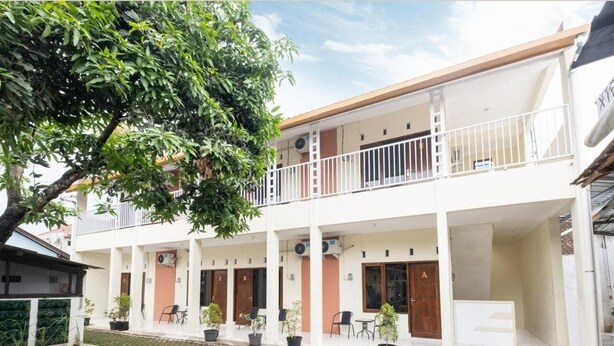 Un immeuble de deux étages doté de nombreux balcons, de plantes en pot et d’une cour dallée.