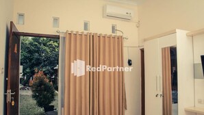 Une pièce dotée d’une porte coulissante donnant sur un jardin, d’une armoire blanche et d’un appareil de climatisation fixé au mur.