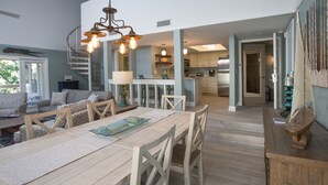 A spacious dining area with a wooden table and chairs, a staircase leading to an upper level, and a kitchen in the background.