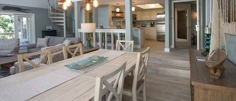 Un vaste espace dédié à la salle à manger, avec une table et des chaises en bois, un escalier menant à un niveau supérieur et une cuisine à l’arrière-plan.