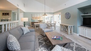 A spacious living area with a sofa, patterned cushions, a wooden coffee table, and a dining table with chairs.