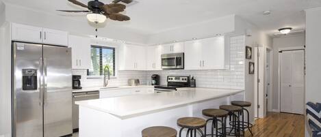A modern kitchen with white cabinetry, stainless steel appliances, a central island with stools, and a ceiling fan.
