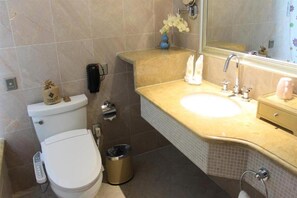 Een badkamer met toilet, bidet, wastafel en spiegel.