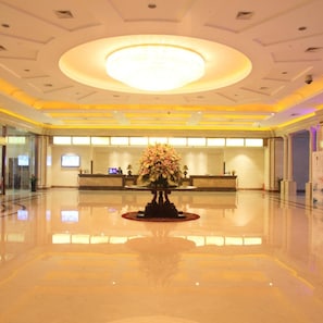A hotel lobby with a reception desk, a large floral arrangement, and a polished floor. - Jinling Huifu Hotel (Yangzhou)