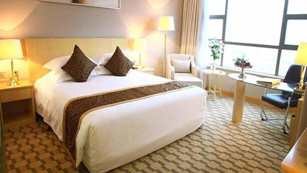 Habitación de hotel con una cama grande, dos mesitas de noche con lámparas, una mesa redonda pequeña con una silla y un ventanal con vistas.