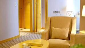 A hotel room with a beige armchair, a round table with a book and a glass, and a door leading to another room. - Jinling Huifu Hotel (Yangzhou)
