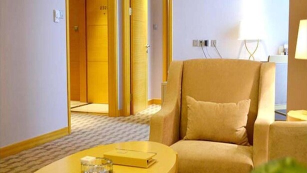 A hotel room with a beige armchair, a round table with a book and a glass, and a door leading to another room. - Jinling Huifu Hotel (Yangzhou)