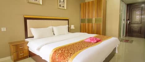 A hotel room with a large bed, a wooden wardrobe, and a door leading to another room.