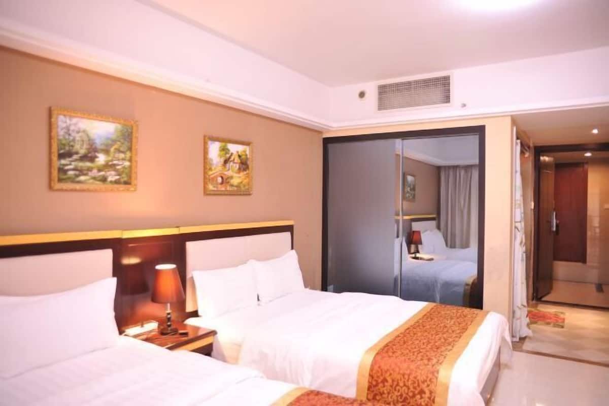 Une chambre d’hôtel avec deux lits, une table de chevet avec une lampe et une porte coulissante donnant sur la salle de bain.